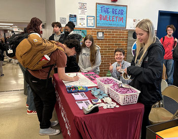 Students interacting at a school club's promotional table labeled 