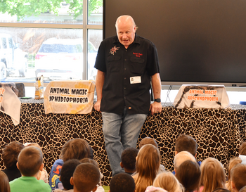 Presenter from Animal Magic speaking to a group of schoolchildren in a classroom setting with a banner reading 'Animal Magic' in the background.