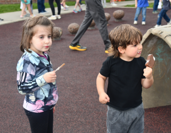 Two children enjoying ice cream at a park, with a play structure in the background.