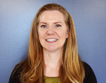 Portrait of a smiling individual with long hair, standing against a blue background.