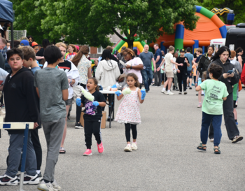 People of various ages enjoying a community fair with street booths and inflatable play structures in the background.