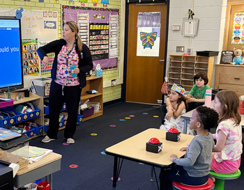 A teacher is presenting a lesson about sleep to young students in a colorful classroom.
