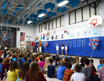 Students gathered in a school gymnasium for an assembly featuring presentations and colorful decorations.