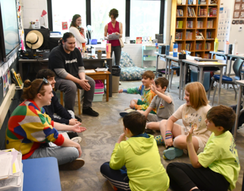 Adults and children sitting on the floor in a circle, interacting in a classroom setting.
