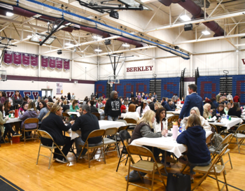 People gathered in Berkley High School's gymnasium, sitting at tables and engaged in conversation during an event.