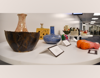 Assorted ceramic artworks displayed on a table, including vases and sculptural pieces, each with an informational tag beside it.