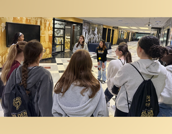 A group of students on a tour, listening to a guide speaking in front of a display