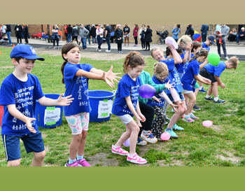 A group of children participating in a balloon toss activity at a school field day, wearing blue t-shirts with