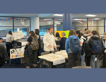 Students and teachers gather around tables at a school event, engaging with educational displays and materials.