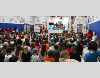 Children attending a school assembly in a gymnasium, watching a performance on a pirate-themed stage.