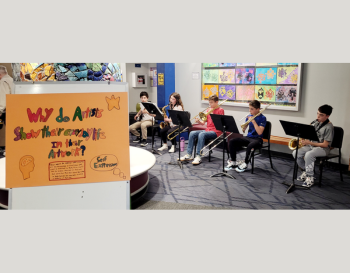 Five young musicians playing brass instruments at a school art exhibit, with colorful artwork in the background