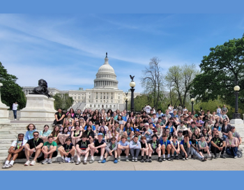 Group of people posing for a photo in front of the United States Capitol building on a sunny day.