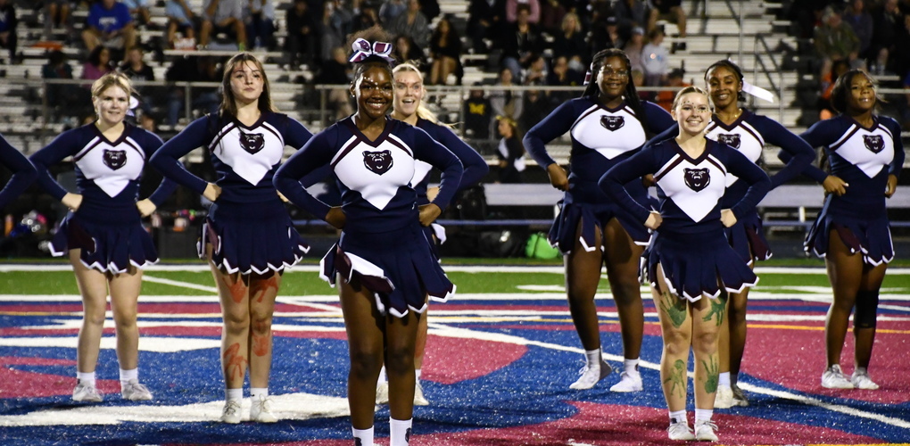 Cheerleaders from Berkley High School standing on a field with a prominent Berkley Bears logo during a nighttime event.