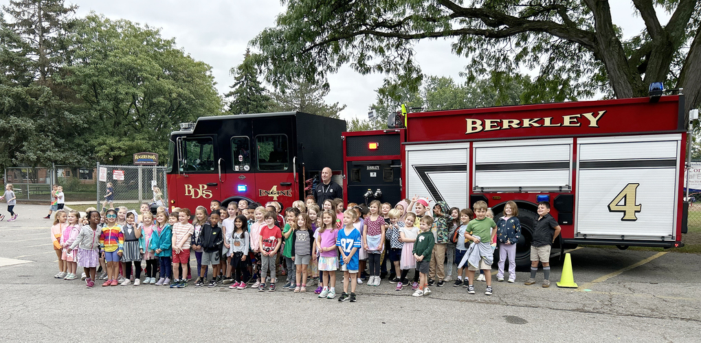 A classroom of students pose in front of a fire truck with a school resource officer standing behind them smiling as well.