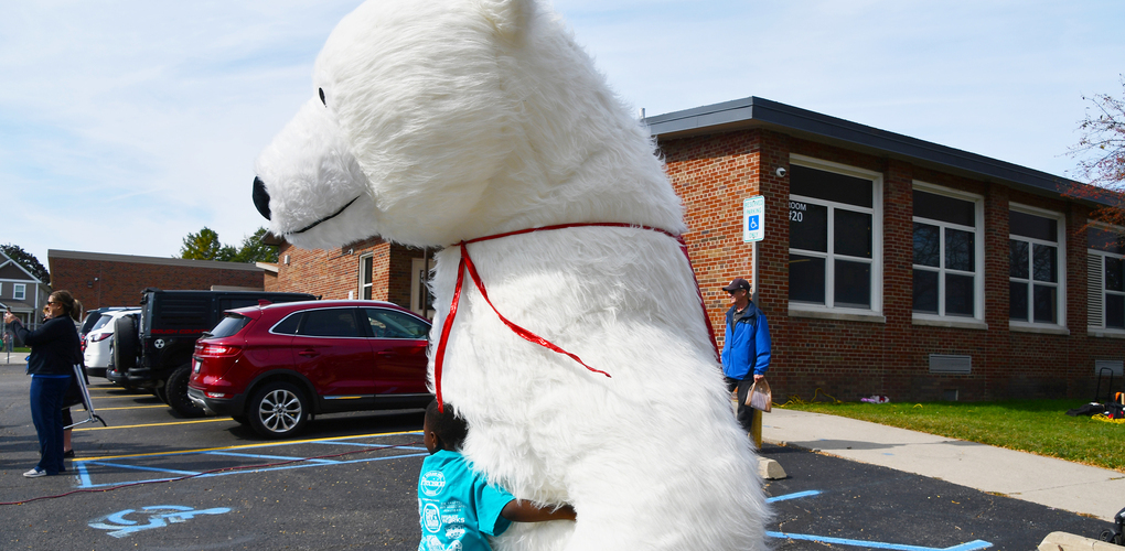 A child interacts with a large polar bear mascot outside a school building.