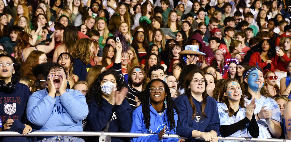 Crowd of enthusiastic fans in a stadium during a night event, many holding banners, cheering and wearing team colors.