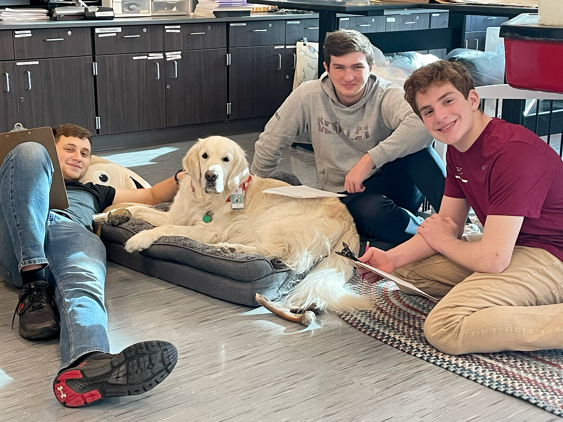 Three individuals posing with a golden retriever in a kitchen, smiling at the camera.